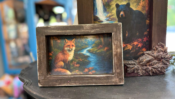 Two framed artworks of a fox and a bear on a dark surface.