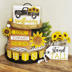 A wooden tiered tray decoration kit with sunflower themes, including cutouts for a truck, sunflowers, and text phrases, arranged on a wooden surface.